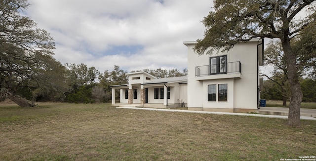 rear view of house featuring a balcony, a yard, and a patio area