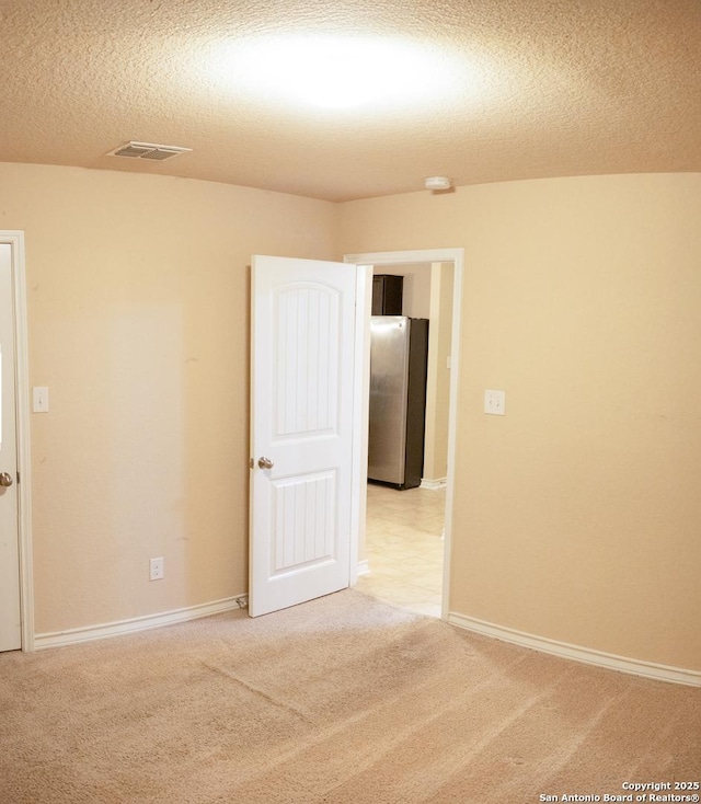 spare room featuring light carpet and a textured ceiling