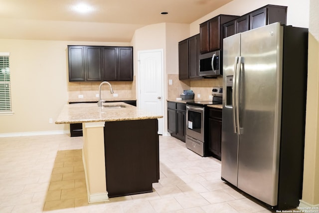 kitchen featuring sink, stainless steel appliances, light stone counters, tasteful backsplash, and a center island with sink