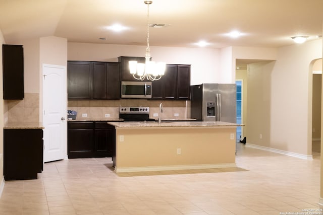 kitchen featuring stainless steel appliances, light stone countertops, a kitchen island with sink, and decorative light fixtures