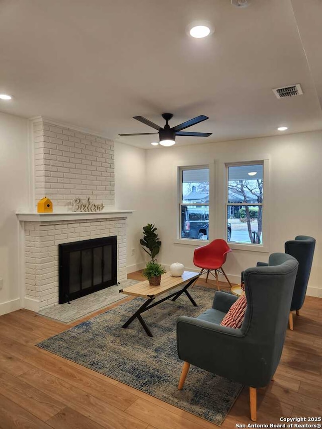 living room featuring wood-type flooring, ceiling fan, and a fireplace