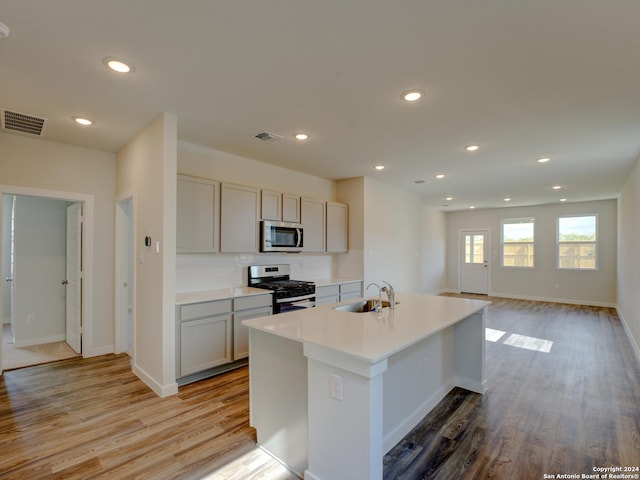 kitchen featuring an island with sink, sink, gray cabinetry, stainless steel appliances, and light hardwood / wood-style flooring