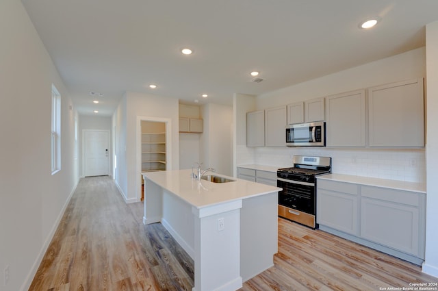 kitchen with appliances with stainless steel finishes, sink, decorative backsplash, a kitchen island with sink, and light hardwood / wood-style floors