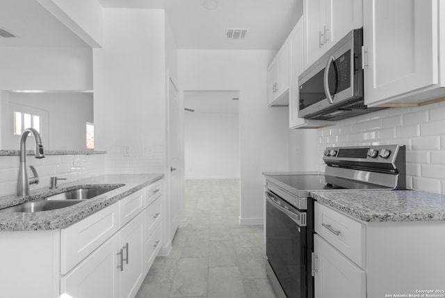 kitchen with appliances with stainless steel finishes, tasteful backsplash, white cabinetry, sink, and light stone counters