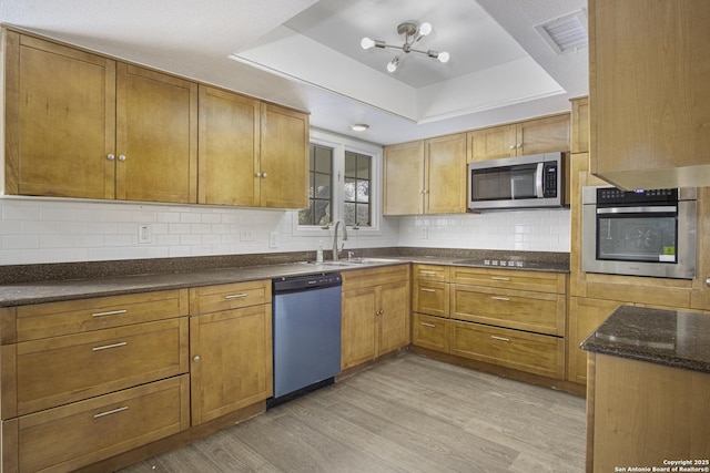 kitchen featuring sink, appliances with stainless steel finishes, tasteful backsplash, light hardwood / wood-style floors, and a raised ceiling