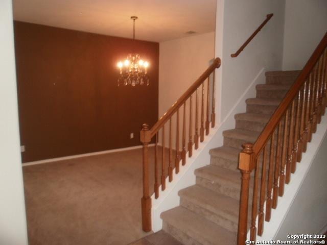 stairway featuring an inviting chandelier and carpet flooring