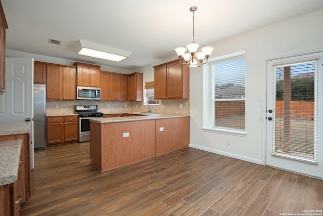 kitchen with dark hardwood / wood-style flooring, kitchen peninsula, pendant lighting, stainless steel appliances, and decorative backsplash