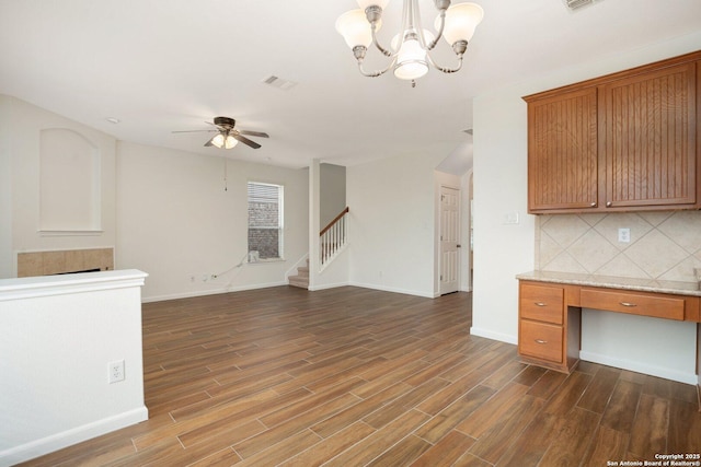 kitchen featuring dark wood-type flooring, hanging light fixtures, tasteful backsplash, built in desk, and ceiling fan with notable chandelier