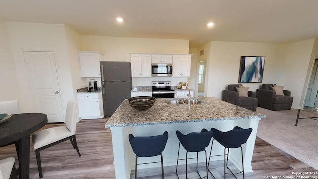 kitchen with white cabinetry, appliances with stainless steel finishes, a center island with sink, and light stone counters