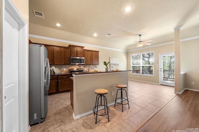 kitchen featuring a breakfast bar, backsplash, ornamental molding, stainless steel appliances, and a center island with sink