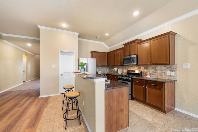 kitchen with appliances with stainless steel finishes, a breakfast bar, tasteful backsplash, an island with sink, and dark stone counters