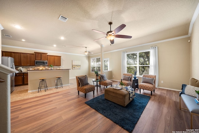 living room with crown molding, ceiling fan, a textured ceiling, and light wood-type flooring