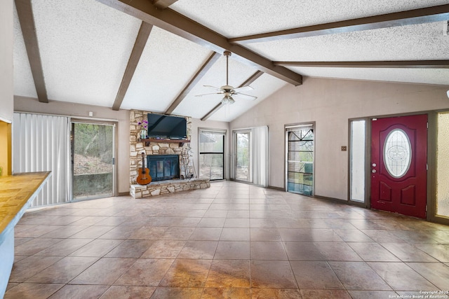 unfurnished living room with vaulted ceiling with beams, a stone fireplace, a wealth of natural light, and a textured ceiling