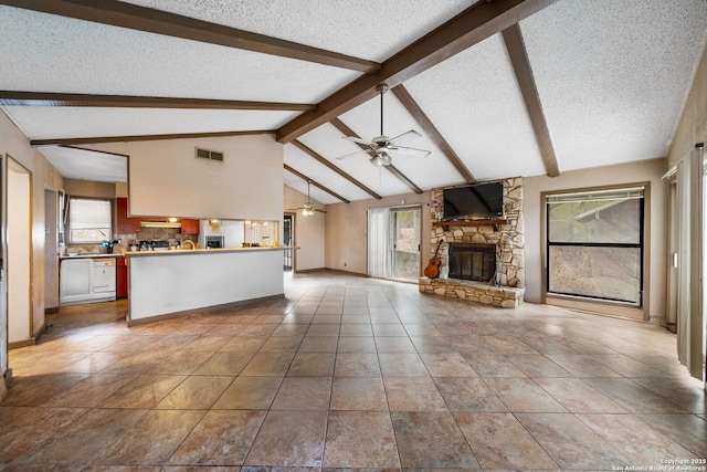 unfurnished living room with vaulted ceiling with beams, a stone fireplace, a textured ceiling, and a wealth of natural light