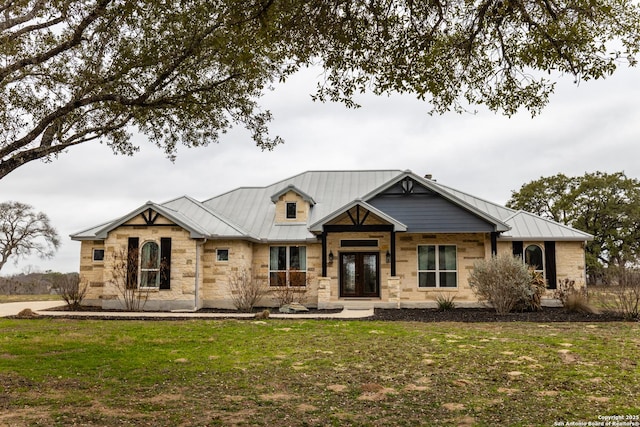 view of front of property with a front yard, stone siding, metal roof, and a standing seam roof