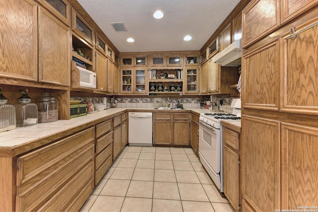 kitchen with sink, light tile patterned floors, tile counters, white appliances, and backsplash