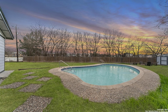 pool at dusk with a storage unit and a lawn