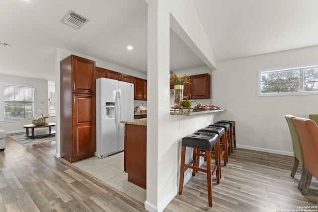 kitchen featuring a breakfast bar, light stone counters, light hardwood / wood-style floors, white fridge with ice dispenser, and kitchen peninsula