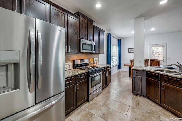 kitchen featuring dark brown cabinetry, sink, appliances with stainless steel finishes, light stone countertops, and backsplash