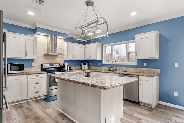 kitchen with wall chimney range hood, sink, stainless steel appliances, white cabinets, and a kitchen island