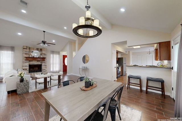 dining area with vaulted ceiling with beams, ceiling fan with notable chandelier, and a fireplace