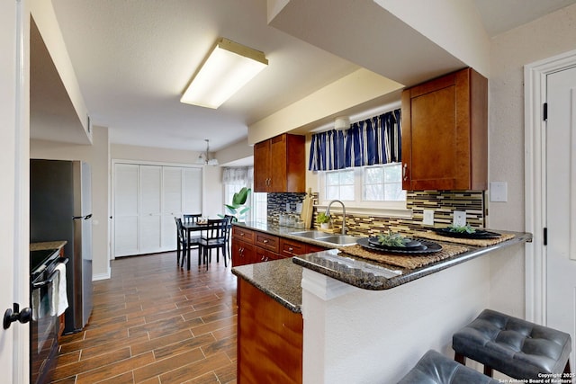 kitchen featuring sink, a breakfast bar area, range, dark stone countertops, and kitchen peninsula