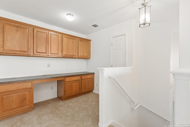 unfurnished office featuring baseboards, built in study area, visible vents, and light colored carpet