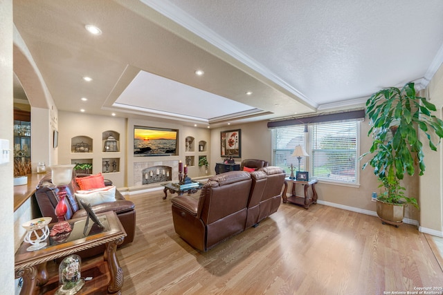 living room featuring crown molding, a textured ceiling, light hardwood / wood-style floors, and a tray ceiling