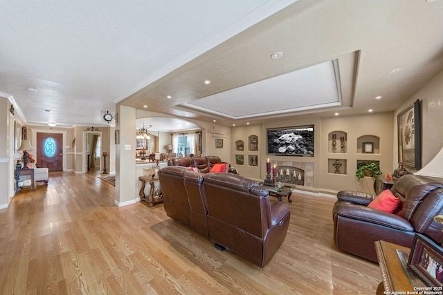 living room featuring ornamental molding, a premium fireplace, a raised ceiling, and light hardwood / wood-style floors