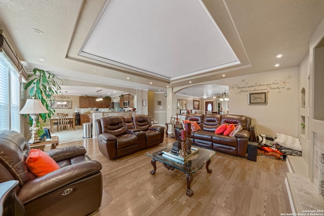 living room featuring a tray ceiling, light hardwood / wood-style floors, a chandelier, and a textured ceiling