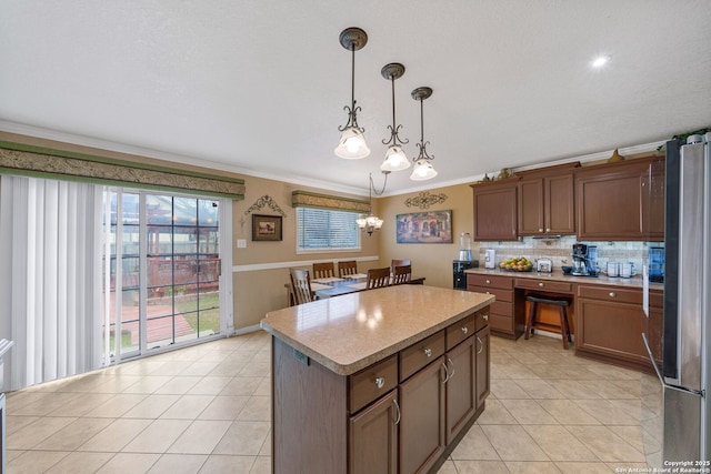 kitchen featuring pendant lighting, stainless steel refrigerator, ornamental molding, a center island, and light tile patterned floors