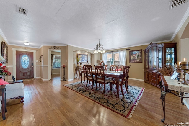 dining room featuring a notable chandelier, ornamental molding, a textured ceiling, and light hardwood / wood-style floors