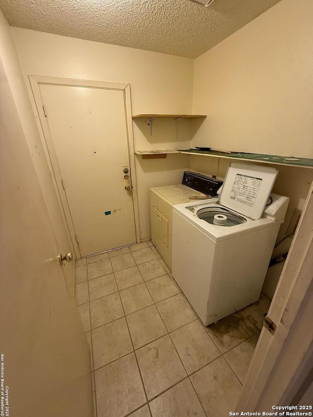 clothes washing area with light tile patterned flooring, washing machine and dryer, and a textured ceiling