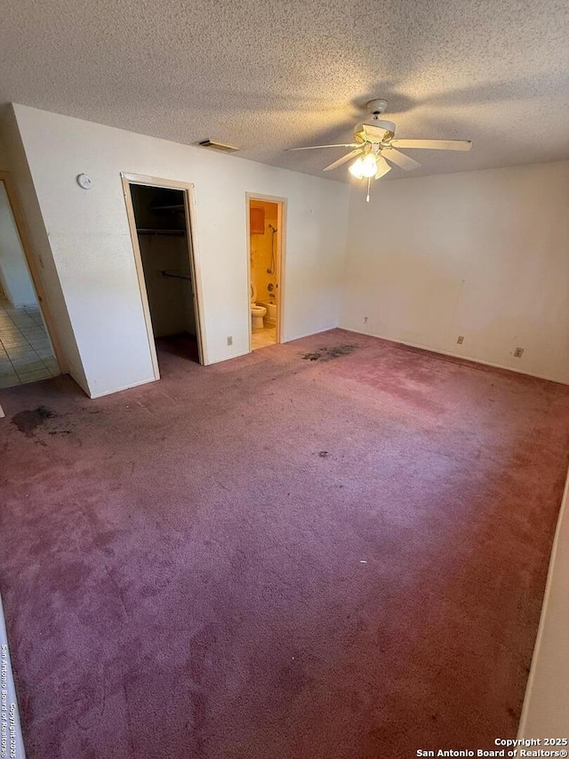 unfurnished bedroom with carpet flooring, a textured ceiling, connected bathroom, ceiling fan, and a walk in closet