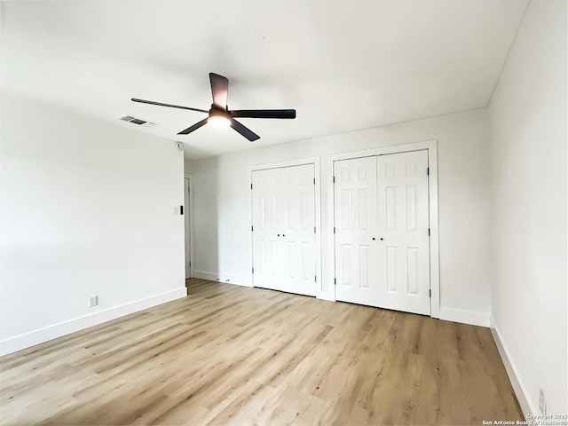 unfurnished bedroom featuring two closets, ceiling fan, and light wood-type flooring