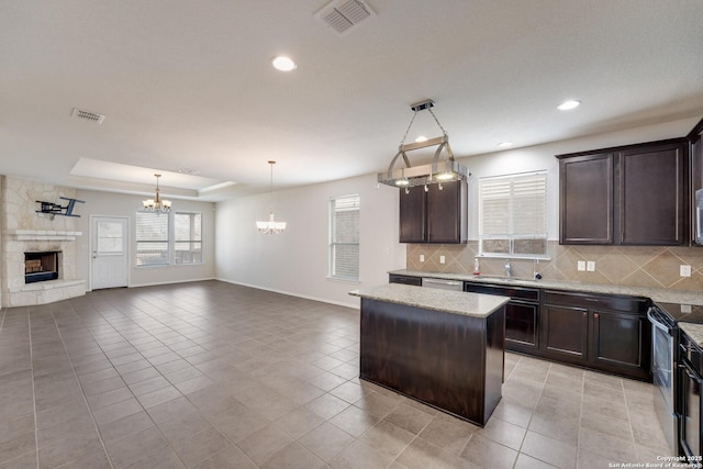 kitchen with a stone fireplace, a tray ceiling, a kitchen island, pendant lighting, and stainless steel appliances