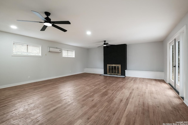 unfurnished living room with hardwood / wood-style flooring, ceiling fan, a brick fireplace, and a wall unit AC