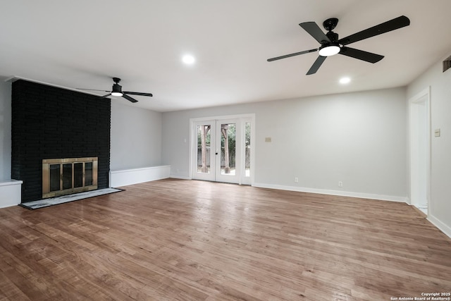 unfurnished living room featuring french doors, ceiling fan, a brick fireplace, and light wood-type flooring