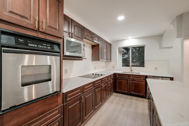 kitchen with sink, tasteful backsplash, light hardwood / wood-style flooring, appliances with stainless steel finishes, and light stone countertops