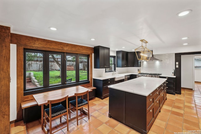 kitchen with a kitchen island, sink, decorative backsplash, hanging light fixtures, and wall chimney range hood