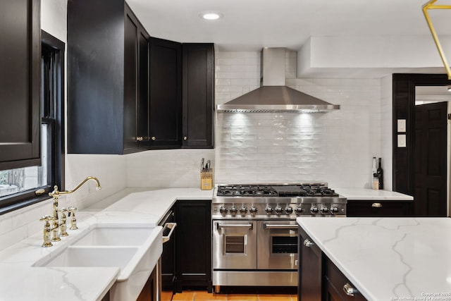 kitchen featuring tasteful backsplash, sink, range with two ovens, light stone countertops, and wall chimney range hood