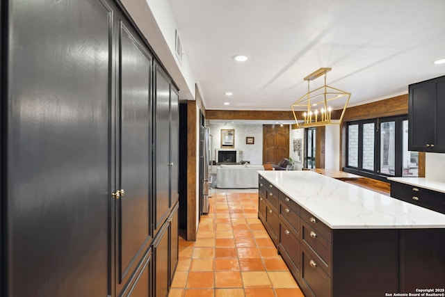 kitchen with decorative light fixtures, stainless steel fridge, a center island, light tile patterned floors, and light stone countertops