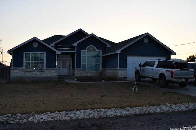 view of front of property featuring a garage, driveway, a lawn, and stone siding