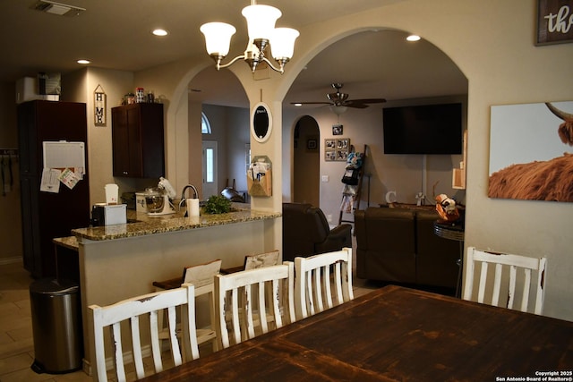 kitchen with arched walkways, light stone counters, ceiling fan with notable chandelier, visible vents, and freestanding refrigerator