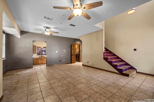 unfurnished living room featuring ceiling fan, light tile patterned floors, and a textured ceiling