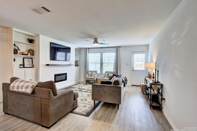 living room with ceiling fan, a fireplace, light hardwood / wood-style floors, and built in features