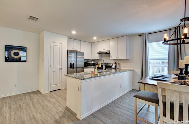 kitchen with appliances with stainless steel finishes, white cabinets, hanging light fixtures, kitchen peninsula, and light stone countertops