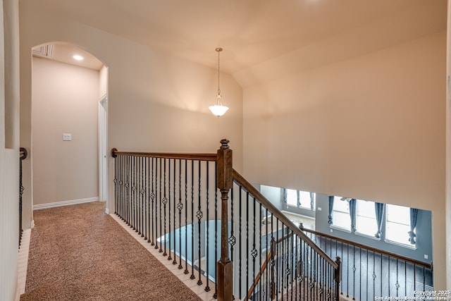 hallway featuring baseboards, arched walkways, vaulted ceiling, an upstairs landing, and carpet floors