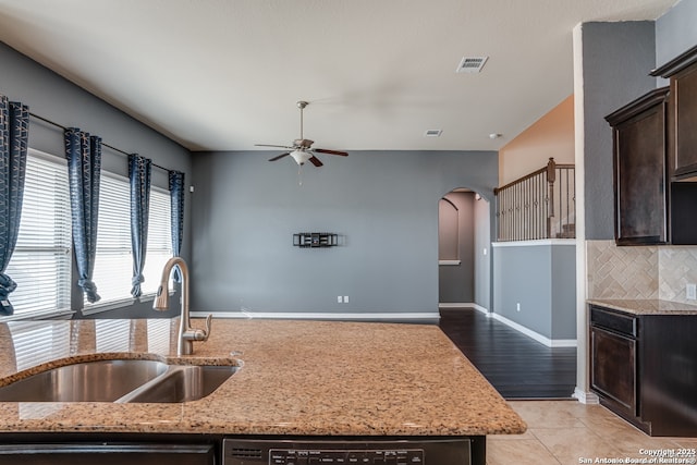 kitchen featuring arched walkways, visible vents, a sink, dark brown cabinets, and light stone countertops