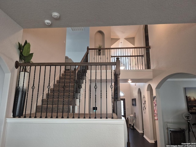 stairway with arched walkways, a high ceiling, a textured ceiling, and baseboards